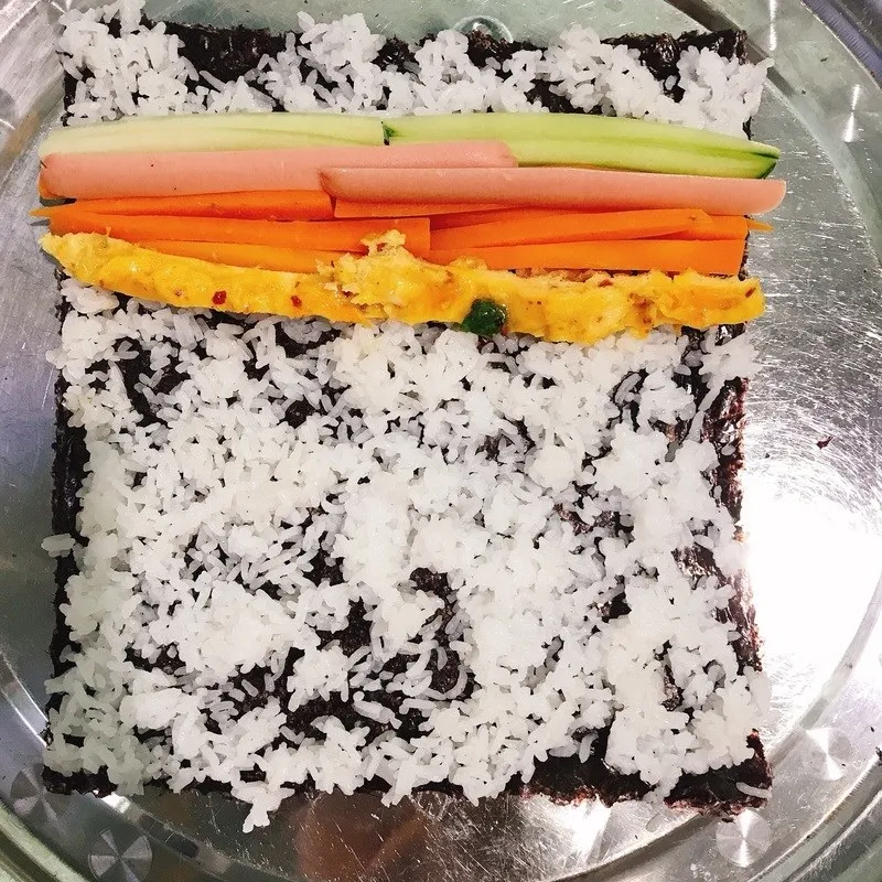 Dùng lực vừa phải để cuộn Kimbap chặt tay giúp các nguyên liệu không bị rơi ra khi cắt