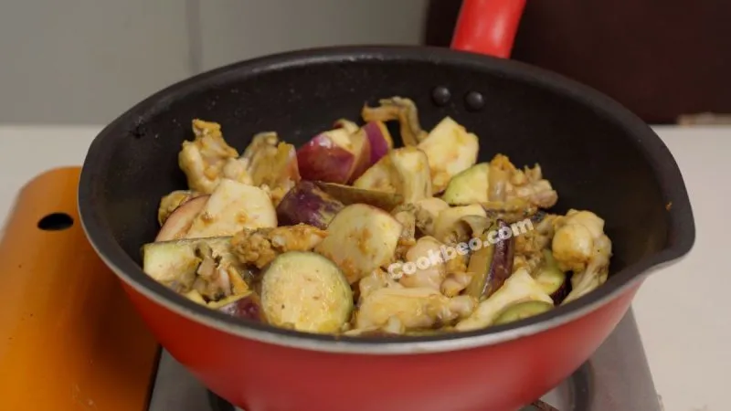 Ếch và cà tím đang được xào chung trên chảo, tạo nên hương vị đặc trưng của món ếch xào cà