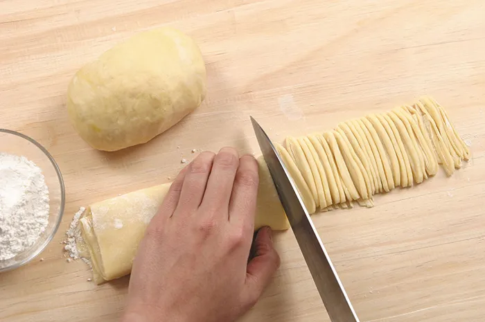 Bột mì sau khi ủ 30 phút được cán mỏng bằng cán gỗ, rắc bột khô, gấp lại và thái thành sợi mì dày 0,2cm