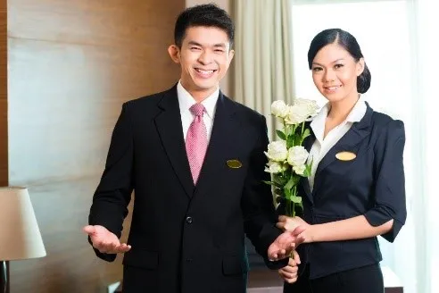 Nhân viên housekeeping chuẩn bị phòng khách theo tiêu chuẩn 5 sao với ga trải giường trắng tinh và khăn tắm xếp nghệ thuật
