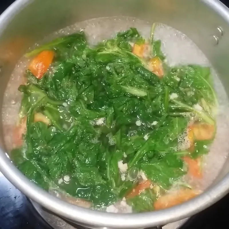 Cho rau cải cúc vào nồi nước đang sôi và nhấn nhẹ để rau được chín đều