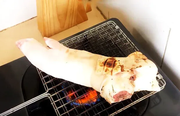 Sơ chế chân giò heo bằng cách thui trên lửa giúp thịt thơm và da giòn hơn